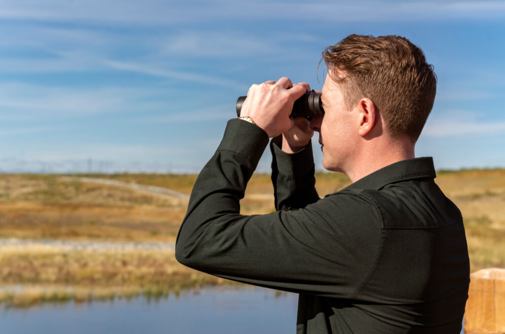 Man looking through binoculars over wetland in Hotchkiss, Calgary